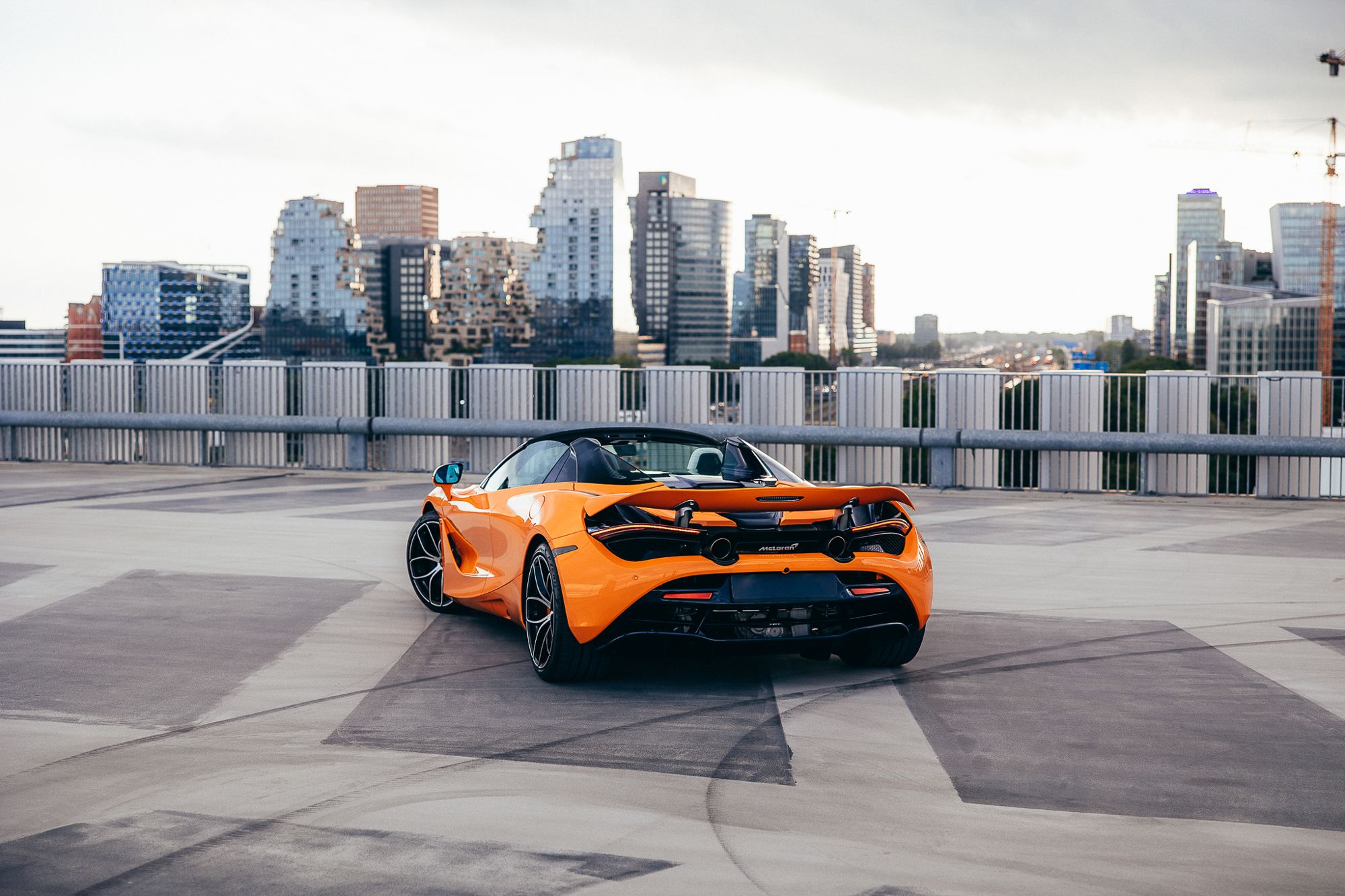 Oranje McLaren 720S Spider op een parkeerdak met skyline